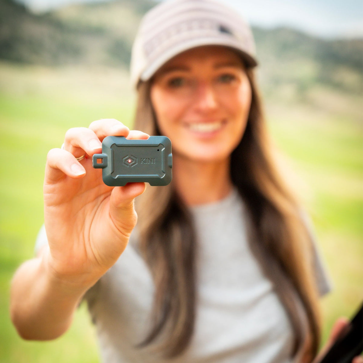 Woman holding a Gun Metal Gray Kini SafeAlert tamper alert device outdoors.