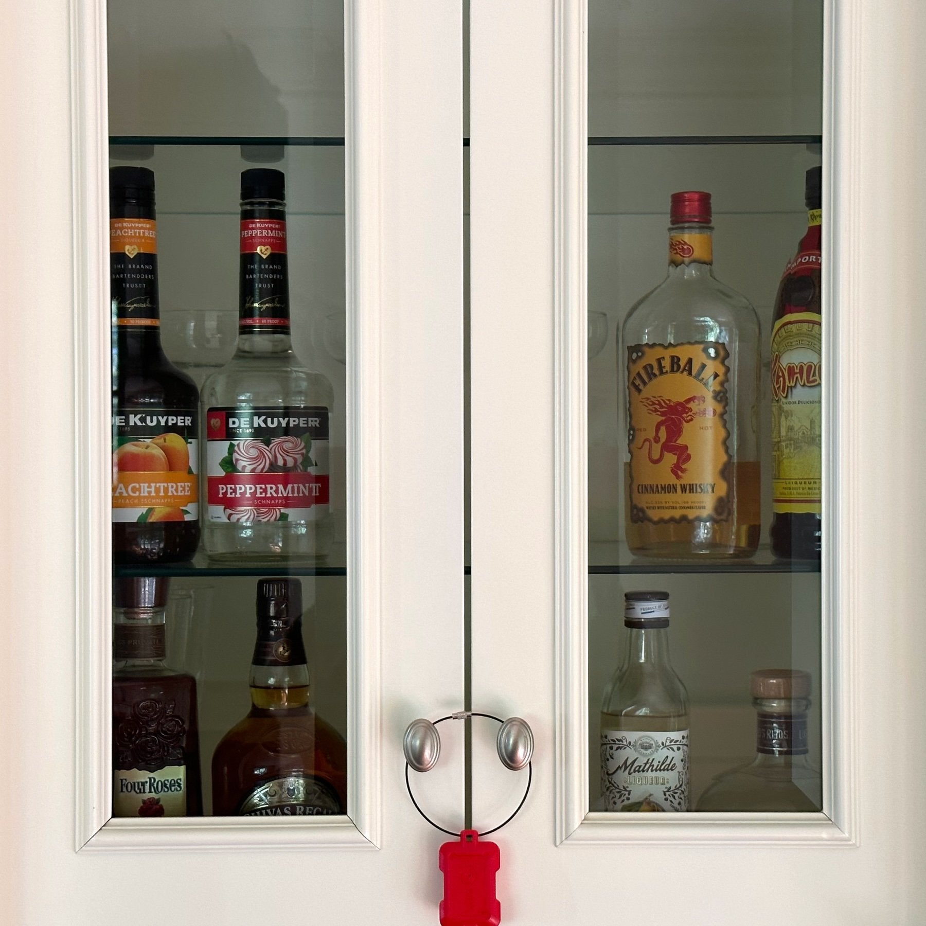 Red Kini Wireless Motion Sensor Hanging from the knobs of a liquor Cabinet  (Mobile)